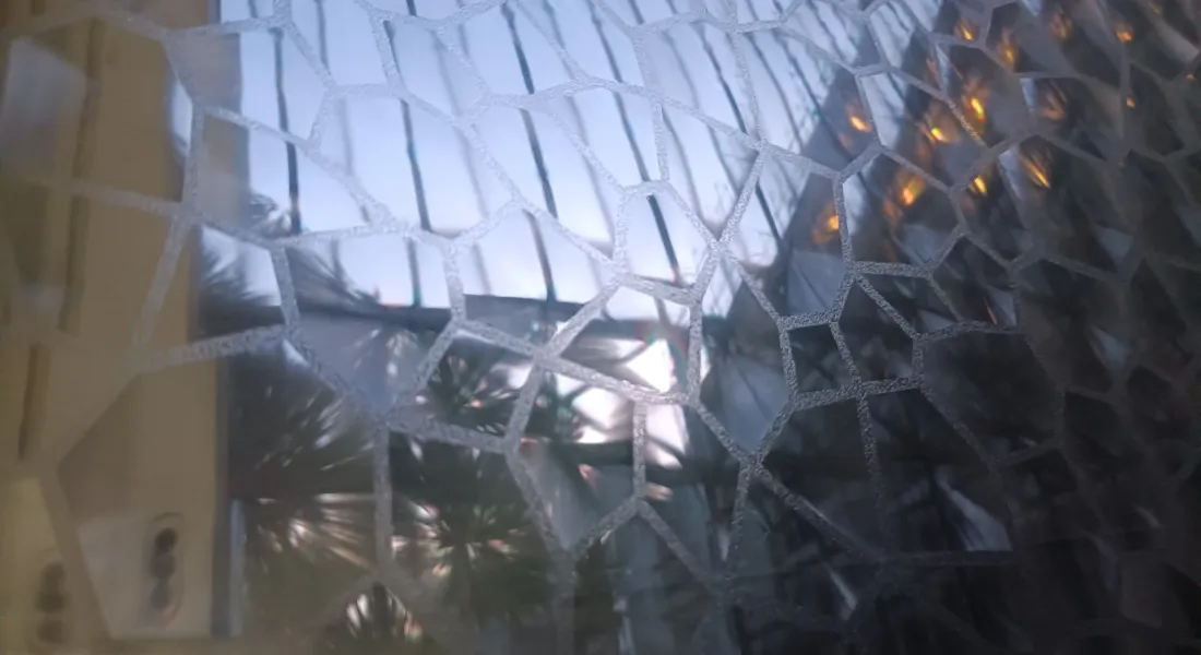 Blick durch ein mit Facettenfolie verhängtes Fenster in einen Innenhof, Abend