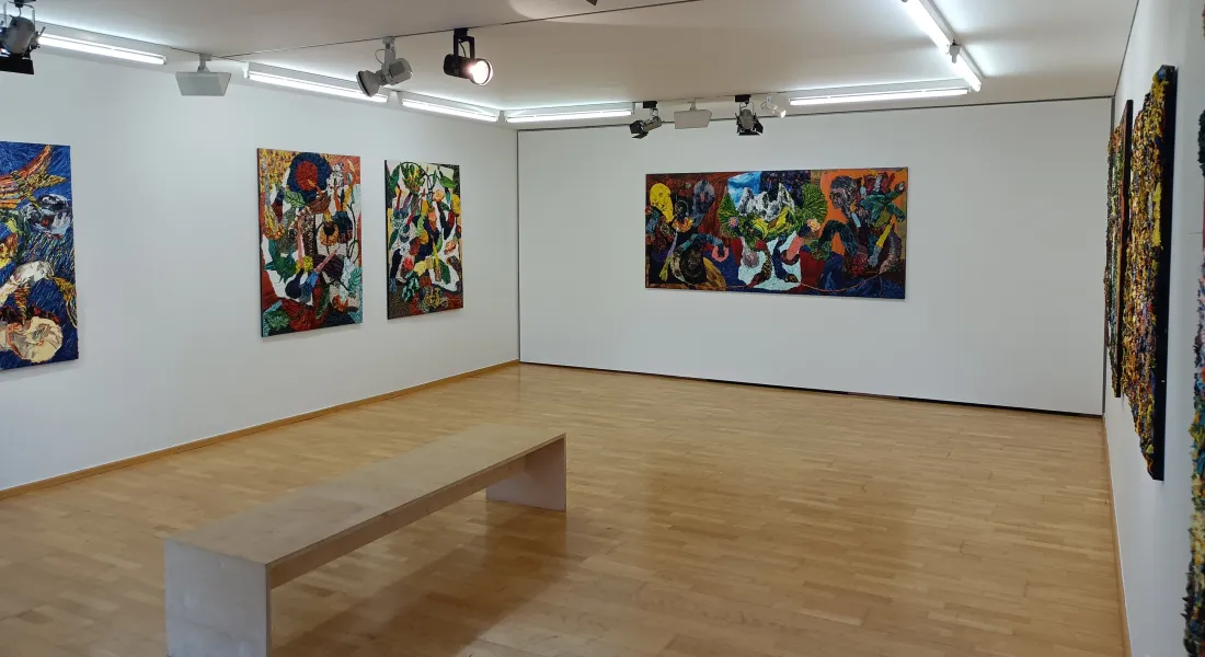 Ausstellungsraum mit Ölgemälden an den Wänden, Scheinwerfern an der Decke und einer Sitzbank in der Raummitte