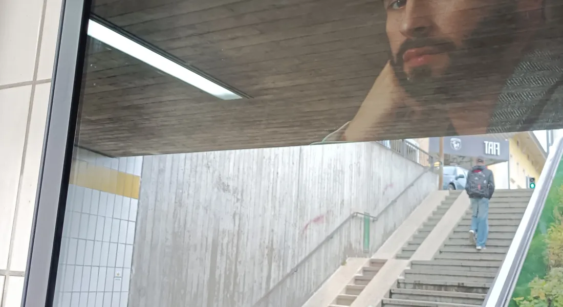 Bild eines jungen Mannes hinter Glas, darin spiegelt sich ein Treppenaufgang zu einer Straße