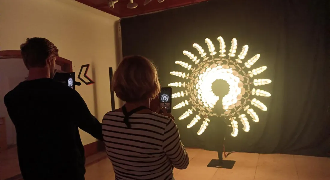 Zwei Menschen (männlich und weiblich) mit erhobenen Smartphones vor einem interaktiven Kunstwerk aus LEDs