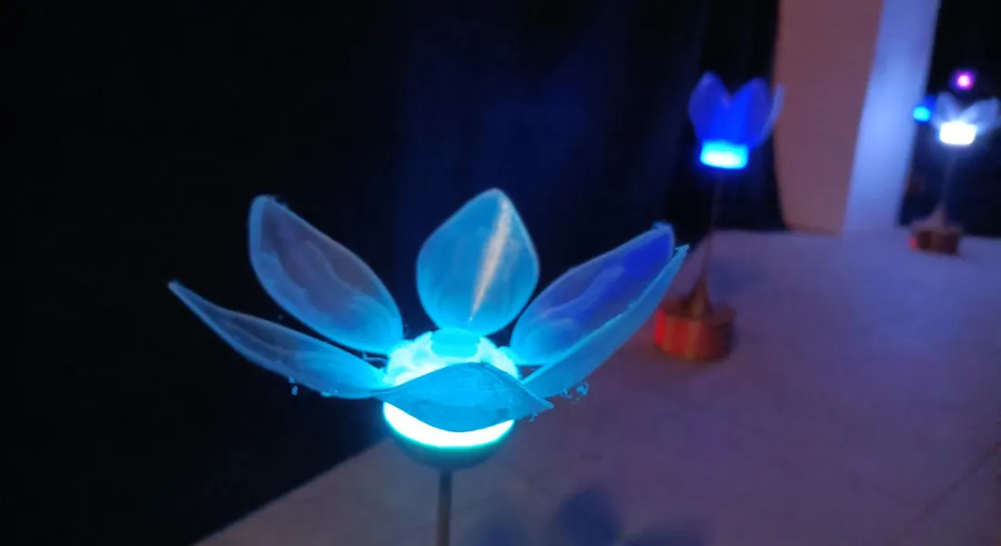 Eine leuchtende künstliche Blume mit weit geöffneter Blüte; im Hintergrund weitere Blumen
