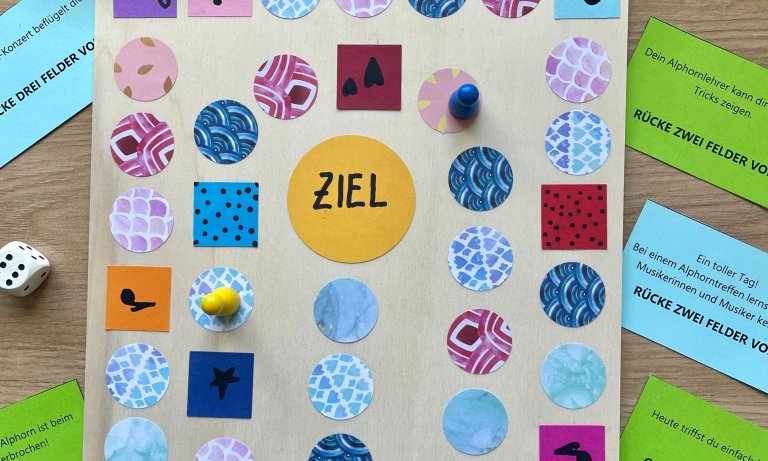 Ein fertig gestaltetes Brettspiel aus Holz mit aufgeklebten Spielfeldern aus buntem Papier.