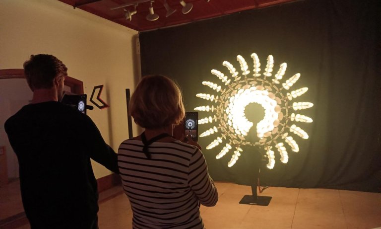 Zwei Menschen (männlich und weiblich) mit erhobenen Smartphones vor einem interaktiven Kunstwerk aus LEDs
